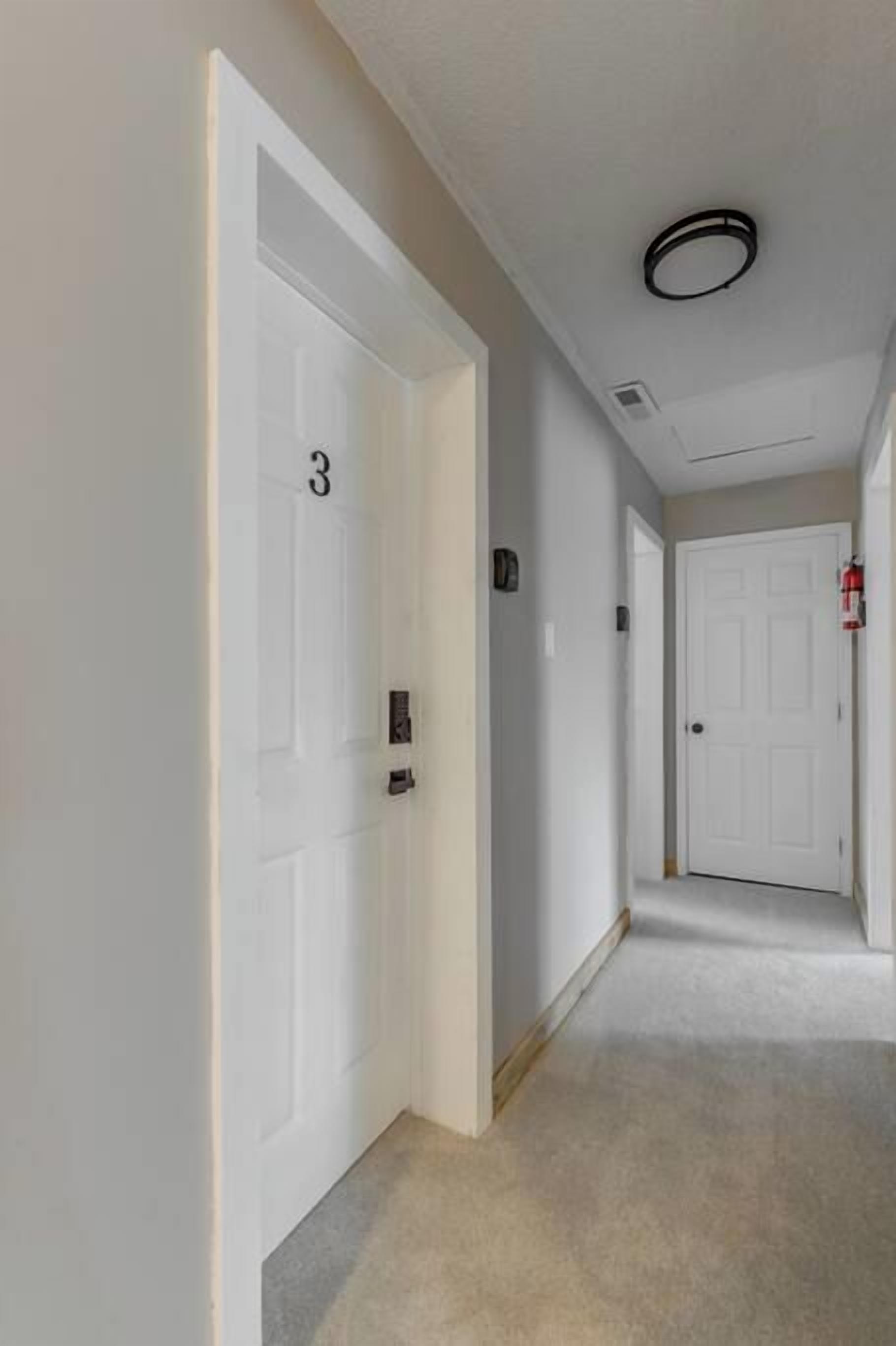 A hallway with white doors, a fire alarm, and a carpeted floor.