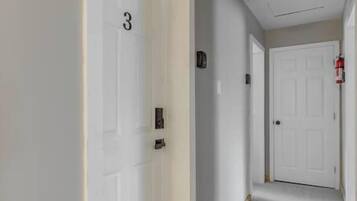 A hallway with white doors, a fire alarm, and a carpeted floor.