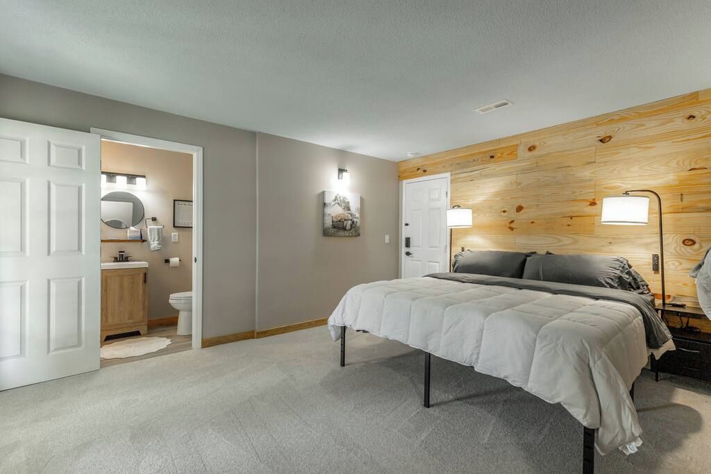 A bedroom with a bed, a wooden headboard, a bedside lamp, and a door leading to a bathroom.