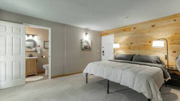 A bedroom with a bed, a wooden headboard, a bedside lamp, and a door leading to a bathroom.