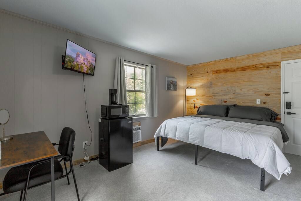 Ein Schlafzimmer mit einem Bett, einem Schreibtisch mit Stuhl, einem Fernseher und einem Fenster mit Vorhängen.