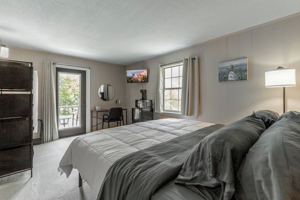 A hotel room with a bed, a desk, a chair, a TV, and a window.