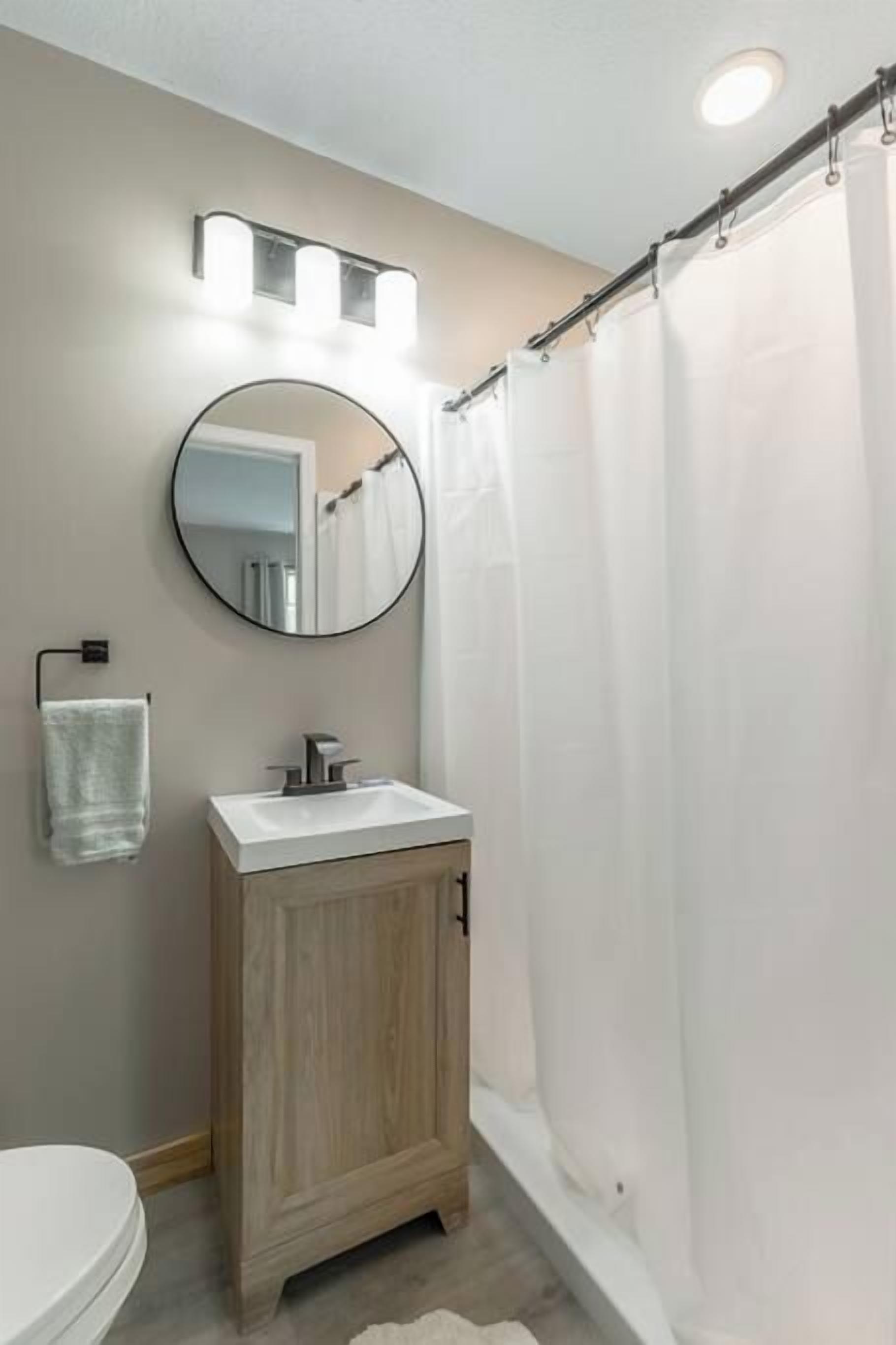 A bathroom with a toilet, a wooden cabinet, a mirror, and a shower curtain.