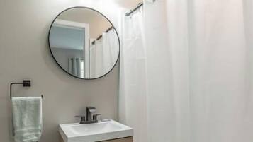 A bathroom with a toilet, a wooden cabinet, a mirror, and a shower curtain.