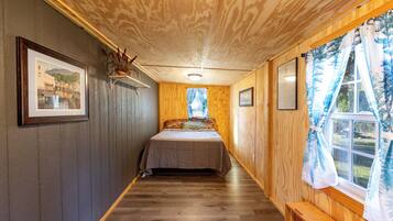 Un estrecho pasillo que lleva a una cama, con suelo y paredes de madera, y una ventana con cortinas.