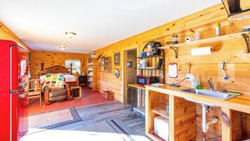 A compact kitchen with wooden walls, a red refrigerator, a wooden dining table with chairs, and a small sink area.