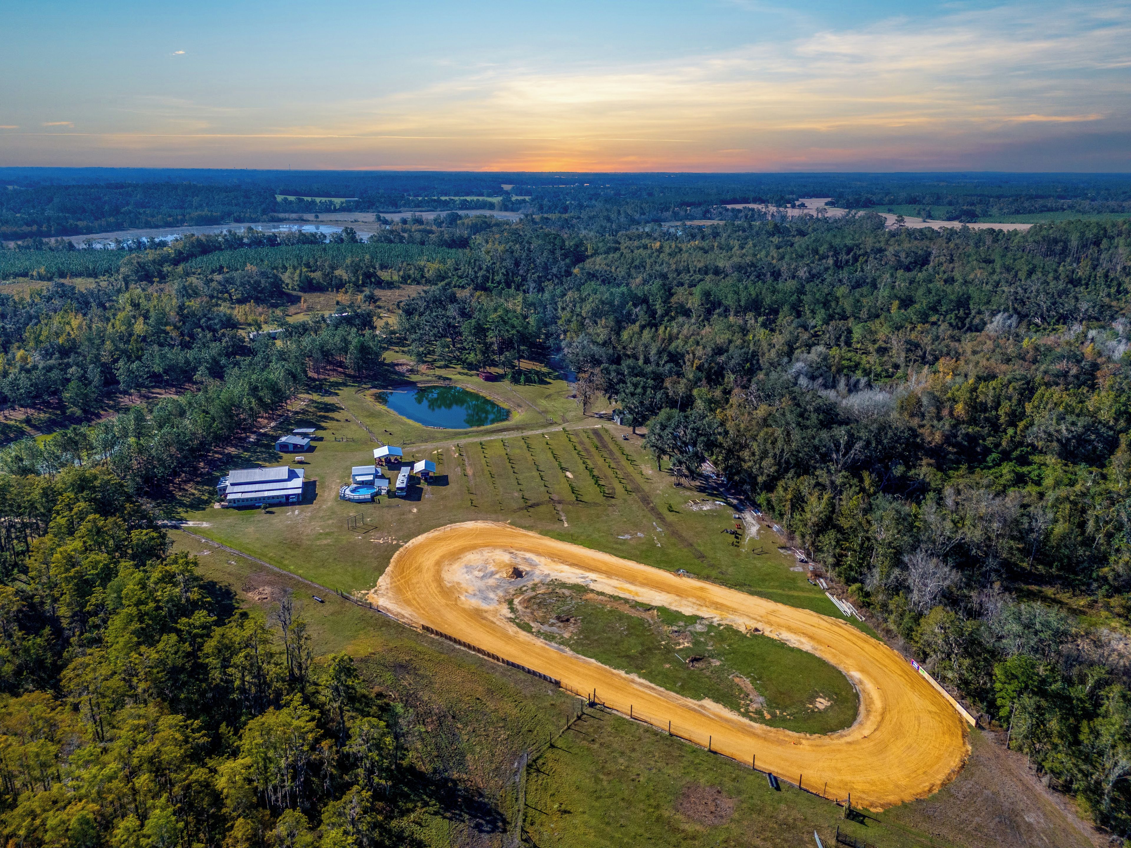 An aerial view of a rural property with a dirt track, a small pond, and scattered buildings.