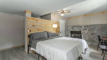 A bedroom with a bed, a ceiling fan, a stone fireplace, and a wooden headboard.
