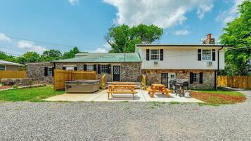 A two-story house with a stone exterior, a patio with picnic tables, and a barbecue grill.