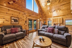A wooden cabin interior with two sofas, a coffee table, and a kitchen area. - Lakefront at Douglas Lake - Private Dock - Hot Tub (Sevierville)
