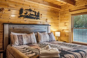 A wooden cabin bedroom with a bed, pillows, a blanket, and a wall decoration. - Lakefront at Douglas Lake - Private Dock - Hot Tub (Sevierville)
