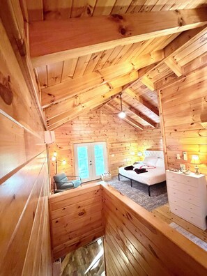 A cozy cabin interior with a loft bedroom, a small seating area, and a wooden staircase.