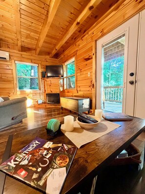 A wooden cabin interior with a sofa, a fireplace, a television, and a table with various items. - Romantic Couples Getaway at Love Shack Cabin - Pet Friendly - Pond Access (Campton)