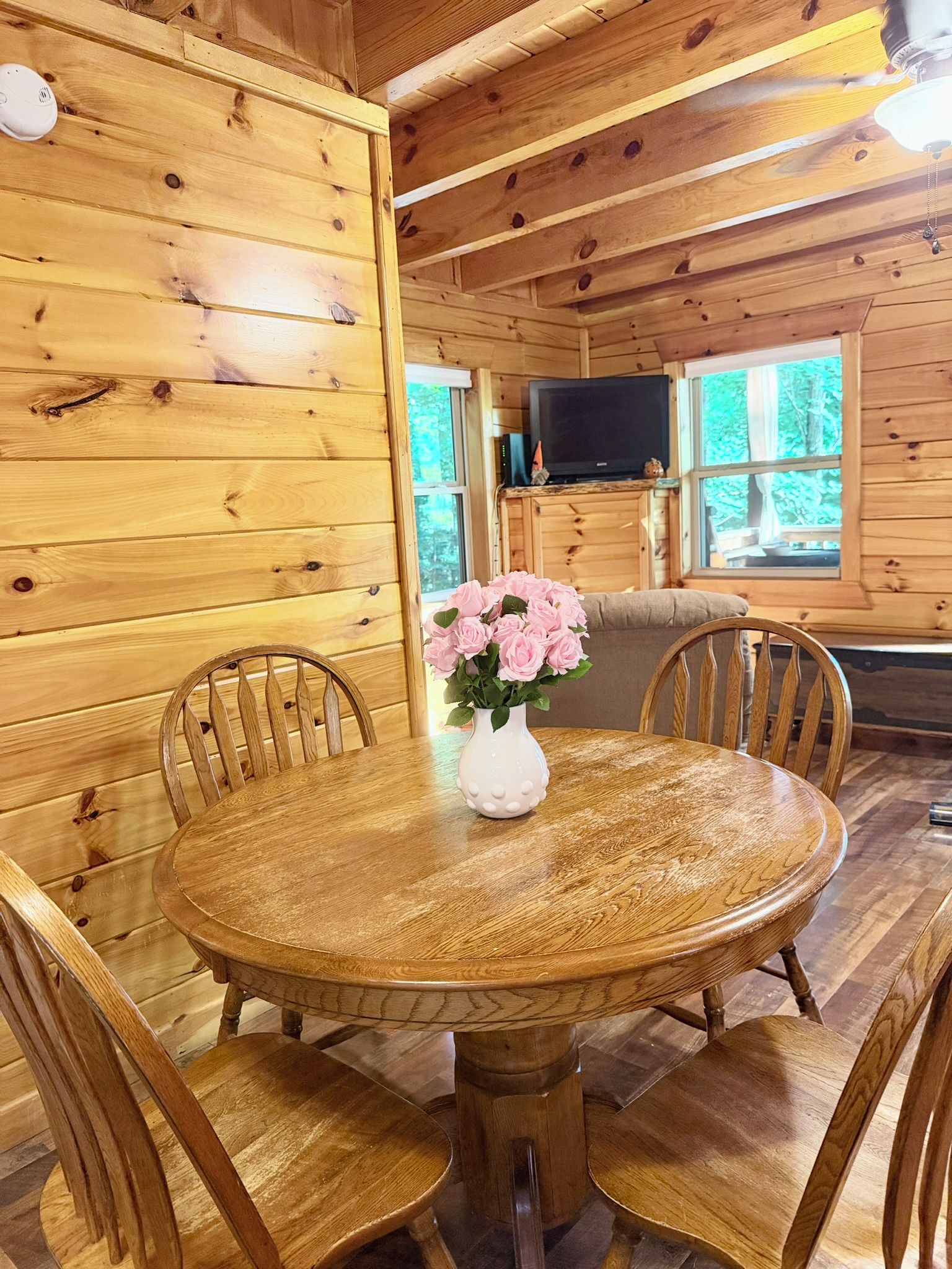 A wooden interior with a round dining table, chairs, and a vase with flowers.