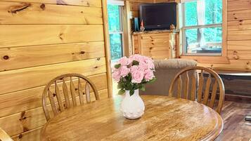 A wooden interior with a round dining table, chairs, and a vase with flowers.