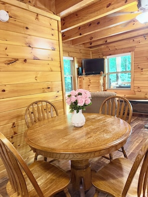 Un interior de madera con una mesa redonda de comedor, sillas y un florero con flores.