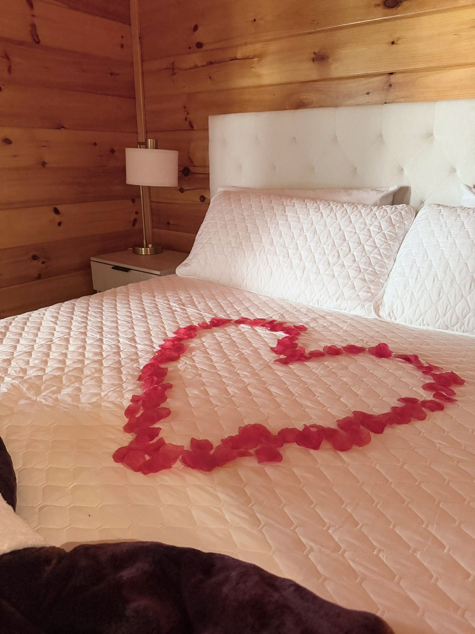 Een bed met een gewatteerd wit hoofdbord en een decoratie in de vorm van een hart, gemaakt van rode stof.