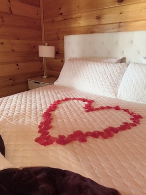 Una cama con cabecera blanca acolchada y una decoración con forma de corazón hecha de tela roja.