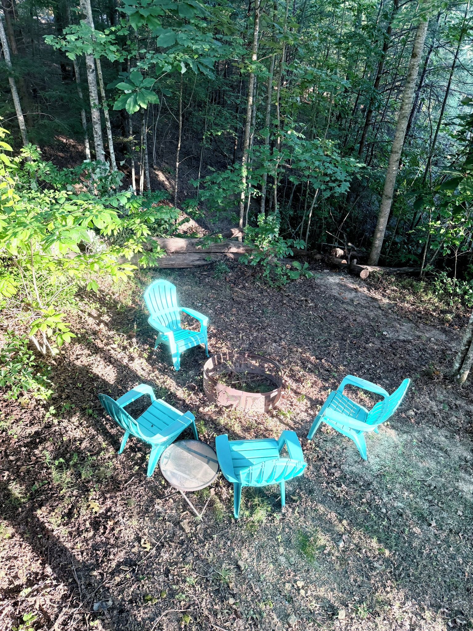 A forested area with a seating arrangement consisting of three chairs and a table.