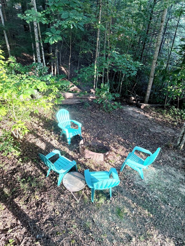 A forested area with a seating arrangement consisting of three chairs and a table.