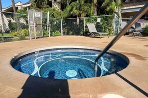 Une piscine dont le fond est recouvert de carreaux, entourée d’une clôture et de palmiers.