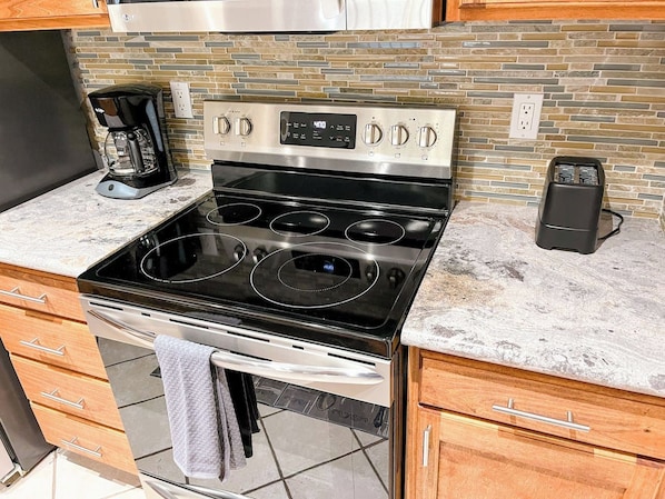 A kitchen with a stainless steel stove, a coffee maker, and a modern tiled backsplash.