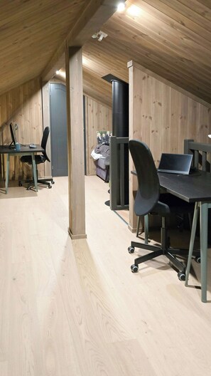 Ein Zimmer mit schragem Dach, Holzwänden, einem schwarzen Heizkörper, einem Schreibtisch mit Stuhl und einem Laptop.