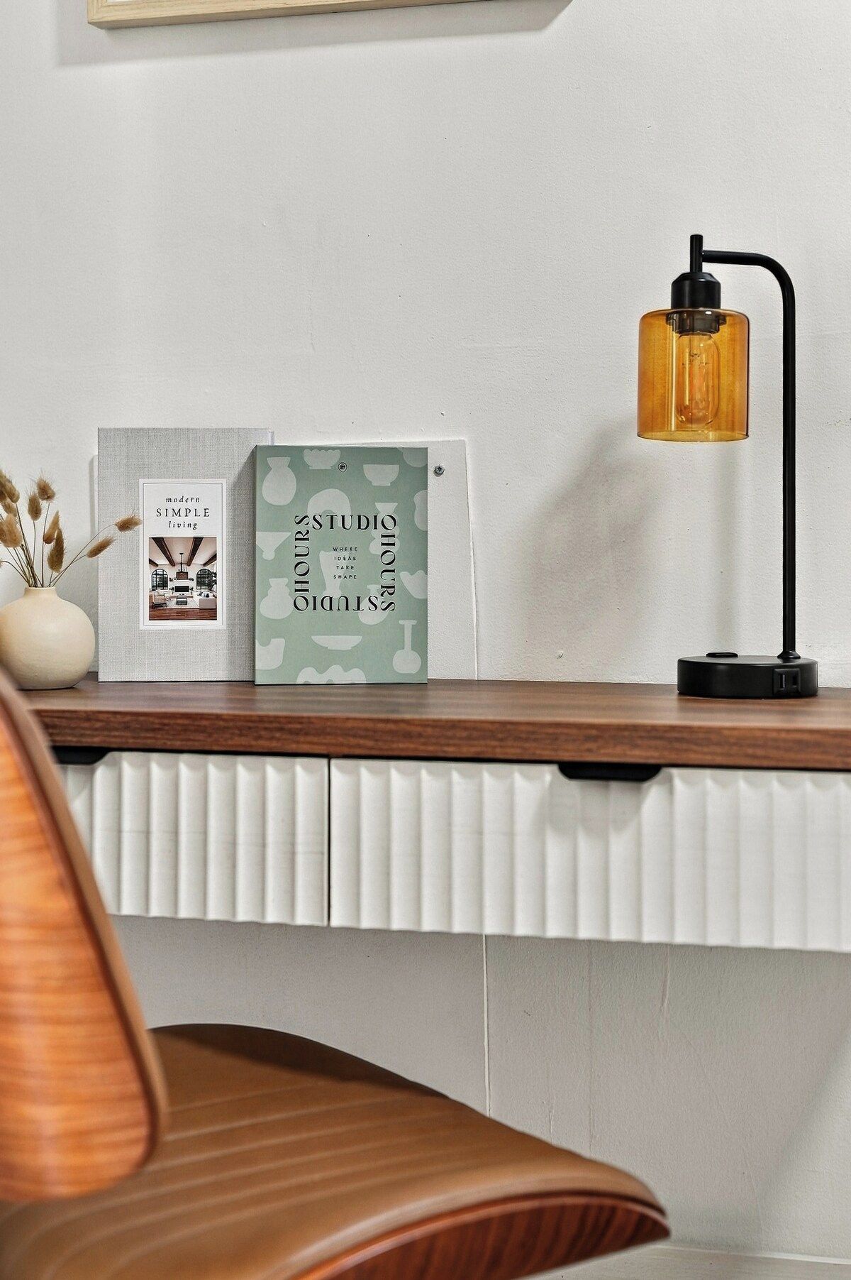 Ett skrivbord med en lampa, en inramad bok och en dekorativ prydnad.