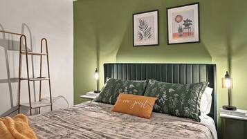 A neatly made bed with a floral-patterned bedspread and a single orange pillow with text.