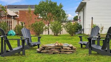 Een achtertuin met twee Adirondack stoelen, een vuurkorf van steen en een huis met bakstenen.