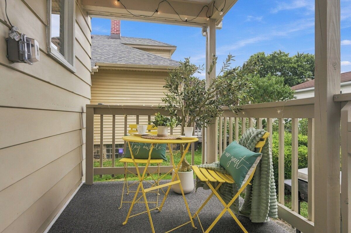 A covered outdoor seating area with a table and chairs, a potted plant, and a bench.