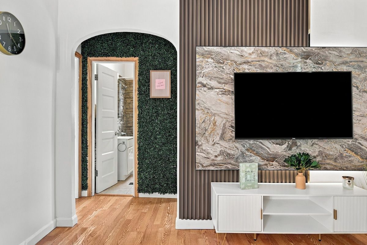 Una sala moderna con un televisor de pantalla plana montado en una pared de mármol, una consola blanca y una pared verde con una puerta que da a otra habitación.