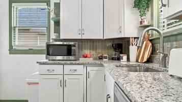 A kitchen with white cabinets, a microwave, a coffee maker, and a sink.