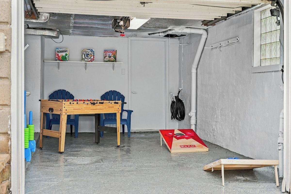 A small room with a foosball table, two blue chairs, a red and white board game, and a window with a view of the outside.