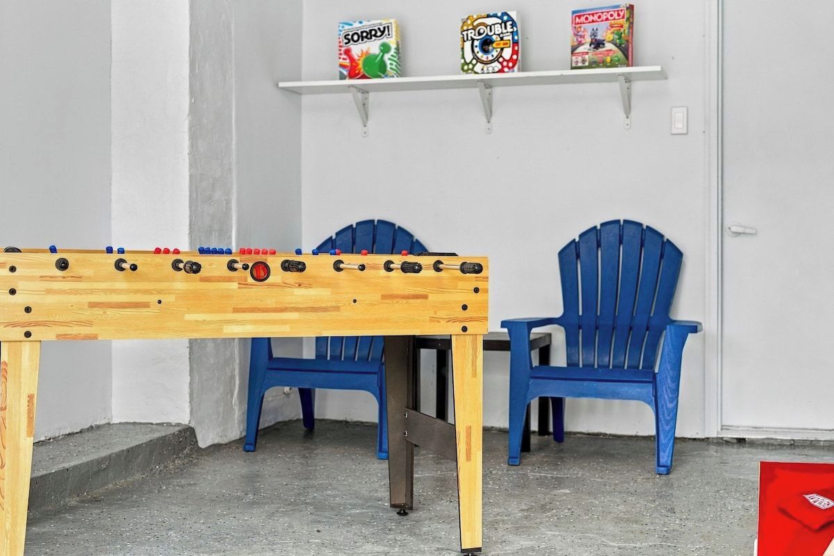 Een kamer met een tafelvoetbaltafel, twee blauwe stoelen en planken met gezelschapsspellen.