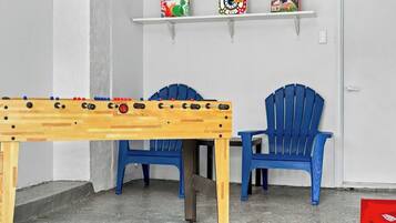 Een kamer met een tafelvoetbaltafel, twee blauwe stoelen en planken met gezelschapsspellen.