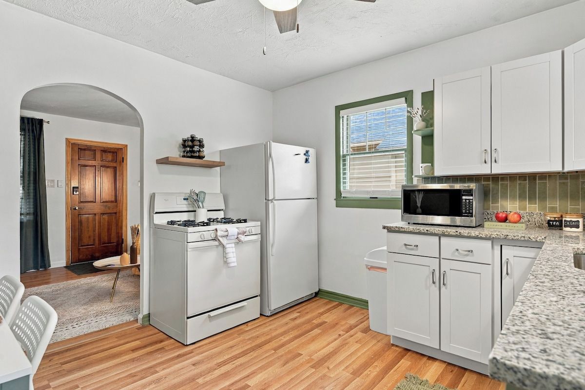 A kitchen with white cabinets, a microwave, a refrigerator, a stove, and a window with blinds.