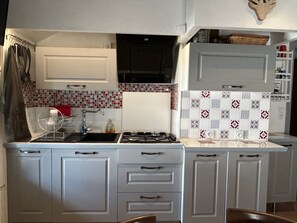 A kitchen with a gas stove, a sink, and a microwave. There are cabinets and a hanging rack. - Charming two-bedroom apartment in the heart of Formiguères (Formiguères)