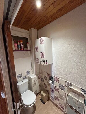 A small bathroom with a toilet, a shelf with toiletries, and a patterned tile backsplash. - Charming two-bedroom apartment in the heart of Formiguères (Formiguères)