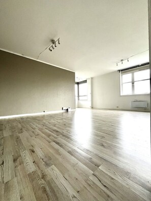 A spacious room with a wooden floor, a large window, and a ceiling light fixture.