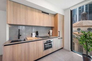 A modern kitchen with wooden cabinets, a built-in oven, and a large window offering a view of a historic building. - 501 First Corner Balcony City Views (Miami)