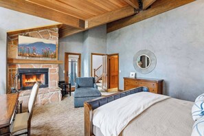 Ein Schlafzimmer mit Kamin aus Stein, einem Bett, einem blauen Sessel und einem Schminktisch.