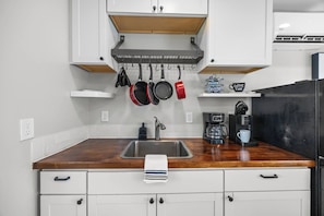 A kitchen with a wooden countertop, a stainless steel sink, hanging pots, a coffee maker, and white cabinets. - Stay Next 2 Duke Hospital, Fire Pit & King Bed (Durham)