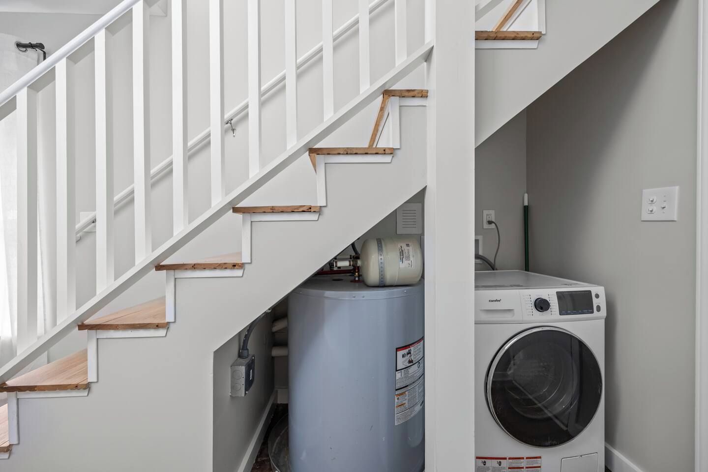 A staircase with white railings and wooden steps leading to a laundry area with a washing machine and a large water heater.