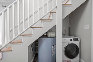 A staircase with white railings and wooden steps leading to a laundry area with a washing machine and a large water heater. - Stay Next 2 Duke Hospital, Fire Pit & King Bed (Durham)