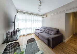 Een moderne woonkamer met een grijze bank, een glazen salontafel en een zwarte fauteuil.