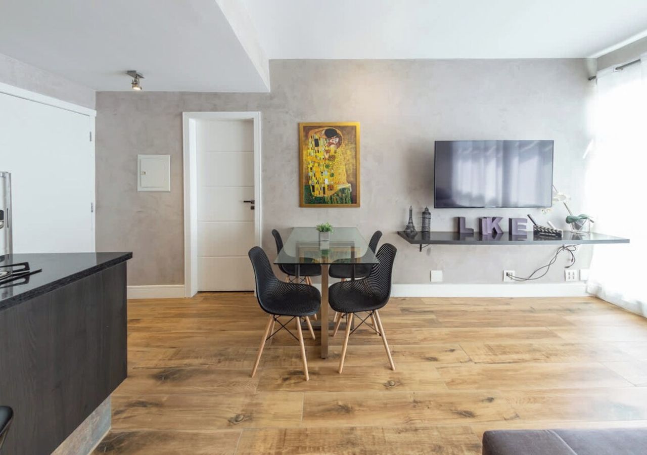 A modern living room with a dining area, a flat-screen TV mounted on the wall, and a wooden floor.