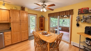 A kitchen with wooden cabinets, a dining table with chairs, a ceiling fan, and a view through a glass door to an outdoor deck. - Lakefront home on Sebec Lake, 4-bedroom, 3 bathrooms (Bowerbank)