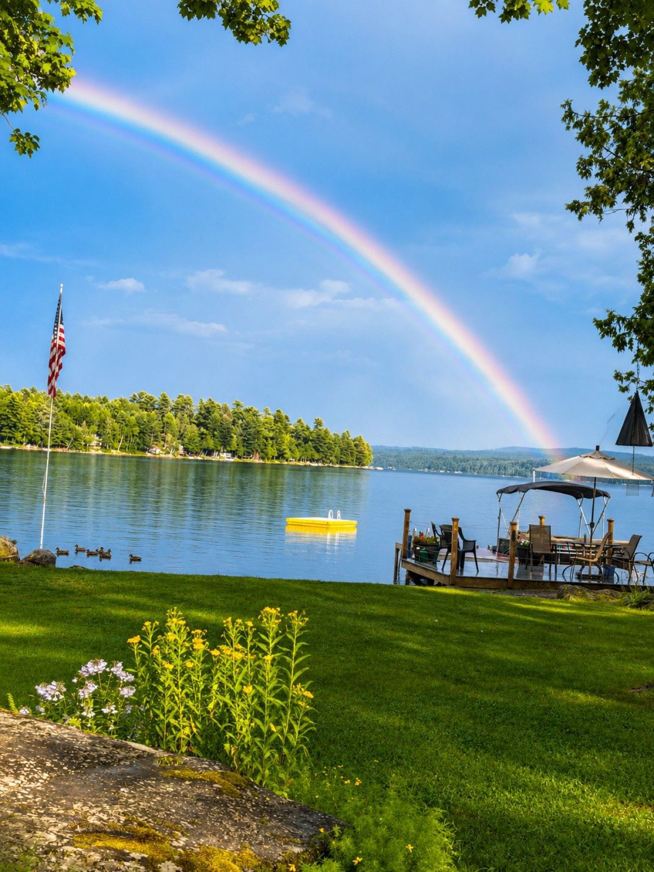 A lakeside view with a rainbow, dock, and outdoor seating area.