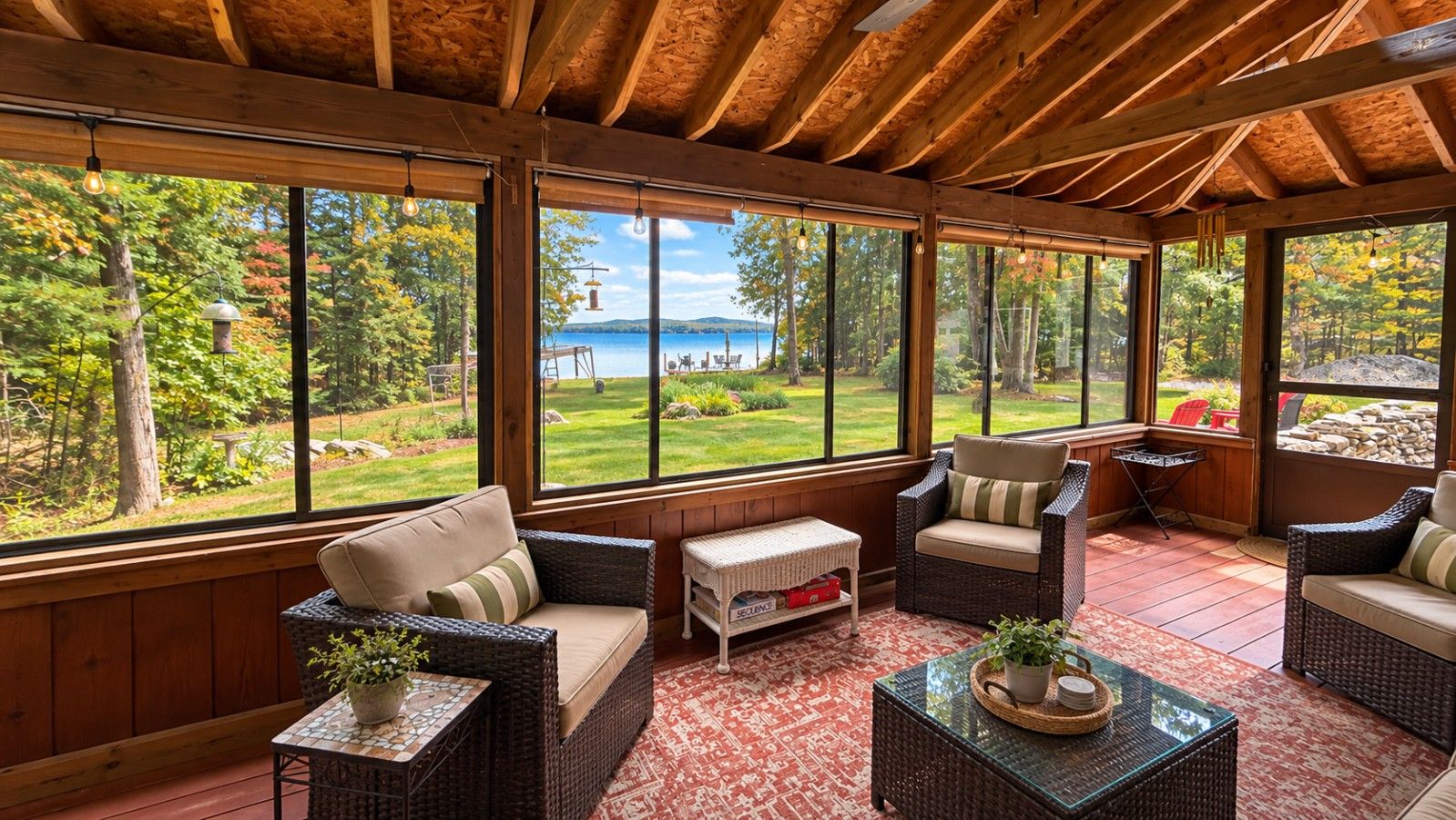 Une véranda meublée de mobilier en osier, dotée de grandes fenêtres et offrant une vue sur un lac.